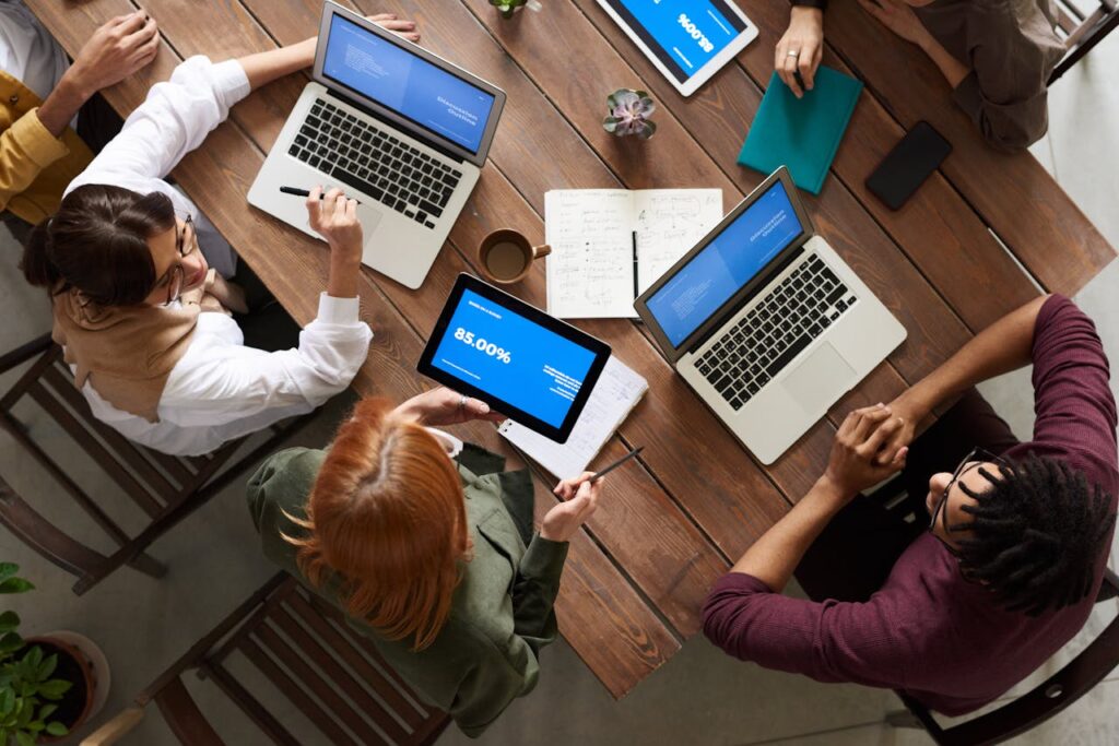 pexels-photo-3182773 Diverse team discussing business strategies with laptops and tablets at a wooden table.